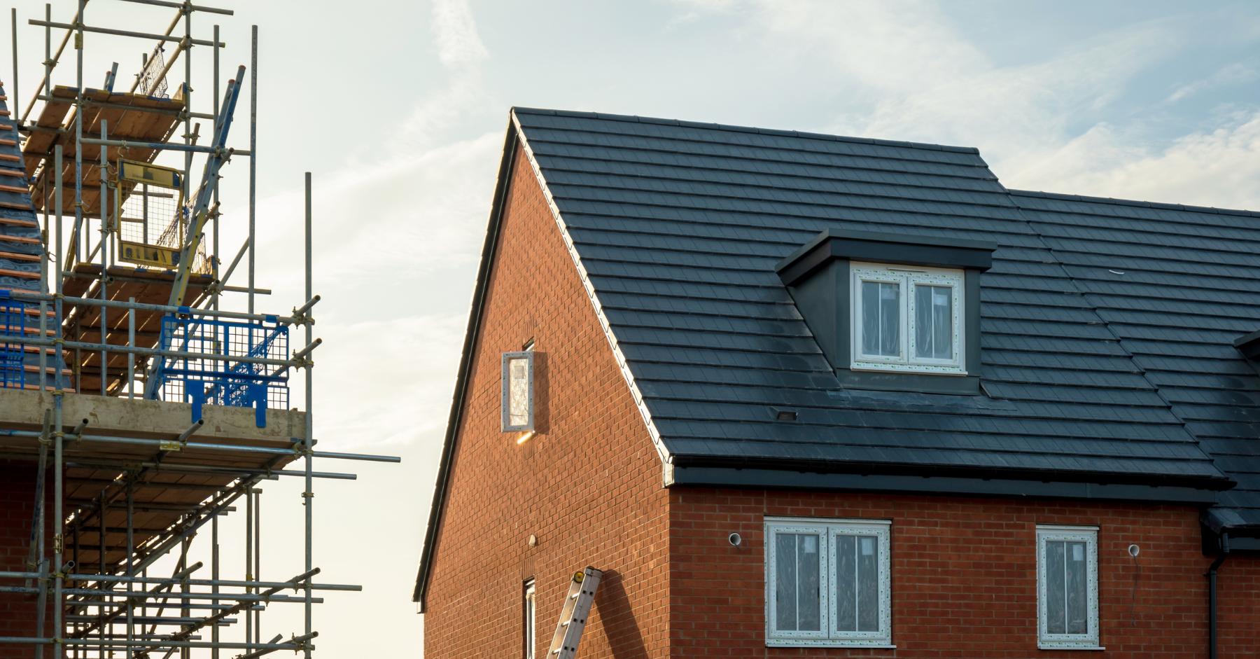 Housebuilding construction sector UK – Newly built brick house with scaffolding beside it on a residential construction site.