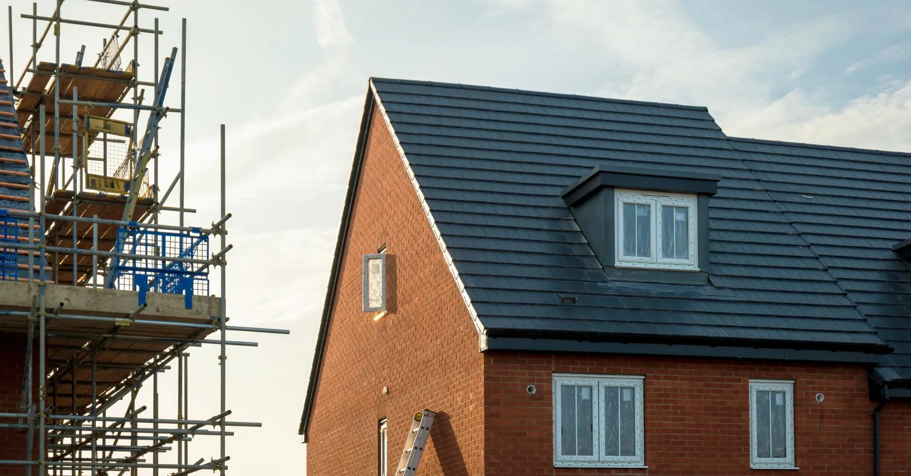 Housebuilding construction sector UK – Newly built brick house with scaffolding beside it on a residential construction site.