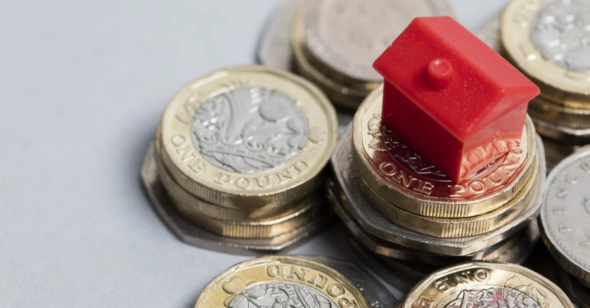 A red, plastic, miniature house on top of a small pile of one pound coins