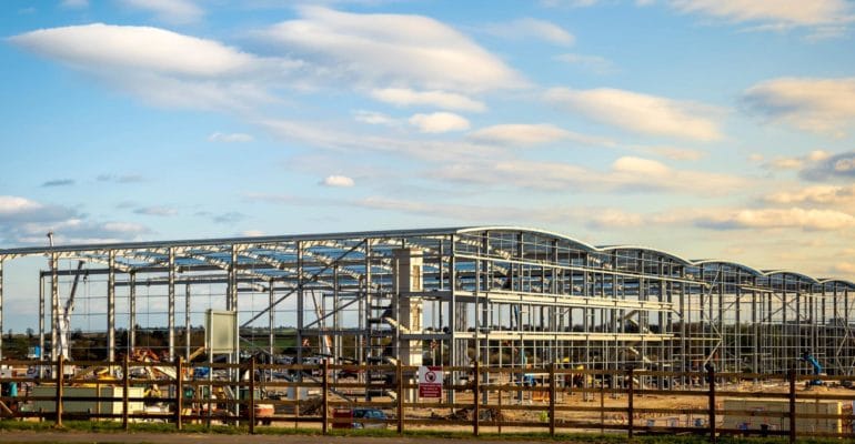 UK construction sector – Large steel frame commercial building under construction on an open development site.