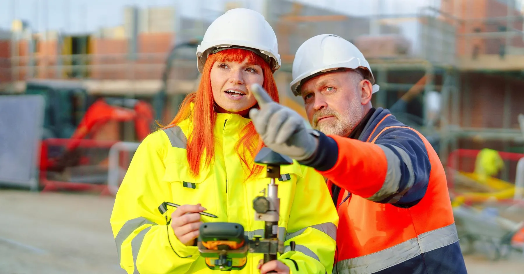 construction training skills gap UK – Two construction workers wearing hard hats and high-visibility clothing discussing plans on a building site.