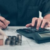 Architect reviewing blueprints and calculating figures to manage project finance effectively.