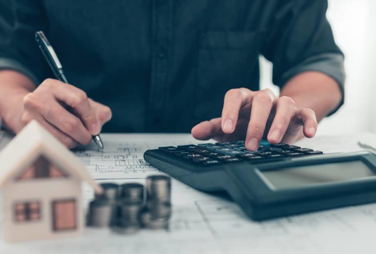 Architect reviewing blueprints and calculating figures to manage project finance effectively.