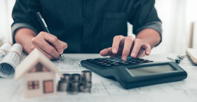 Architect reviewing blueprints and calculating figures to manage project finance effectively.