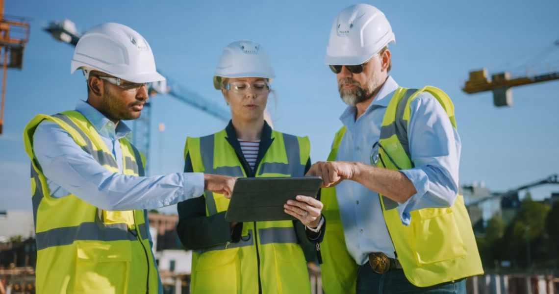 A diverse team of construction workers using a tablet outside.