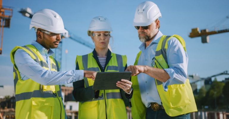 A diverse team of construction workers using a tablet outside.