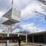 Workers using a crane to install a prefabricated modular building on a building site.