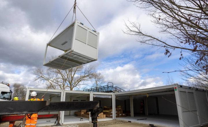 Workers using a crane to install a prefabricated modular building on a building site.