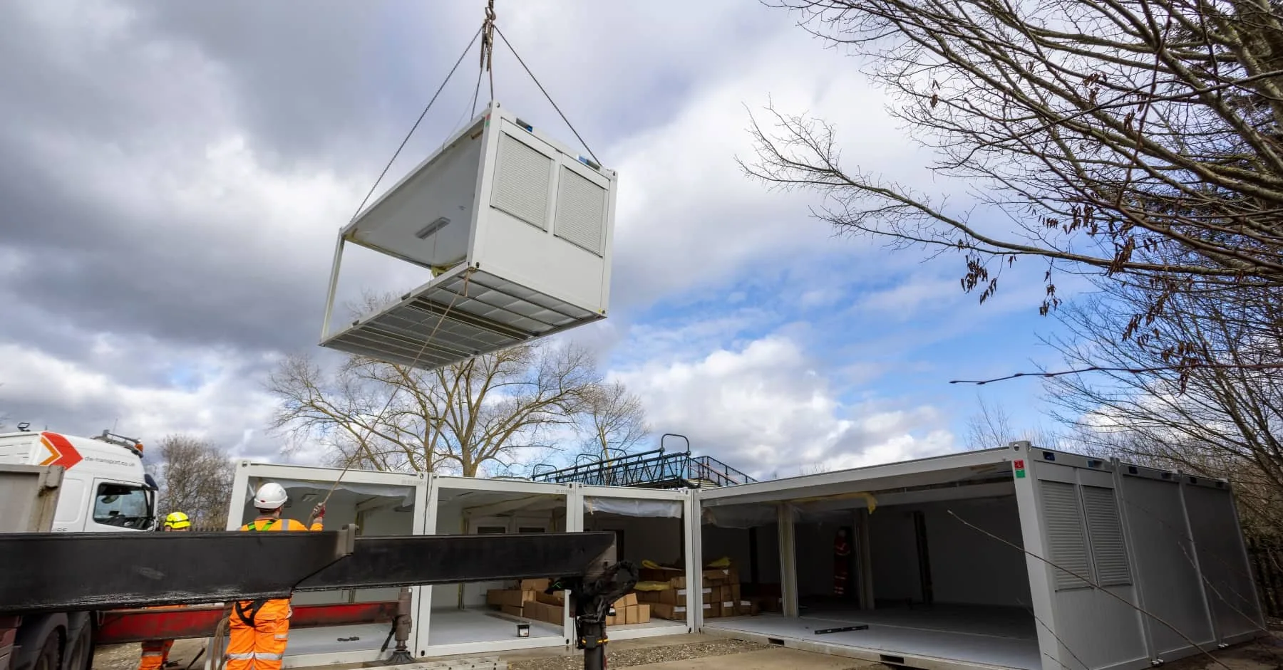 Workers using a crane to install a prefabricated modular building on a building site.