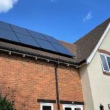 Residential house with brick and cream exterior featuring solar panels installed on the roof under a clear blue sky