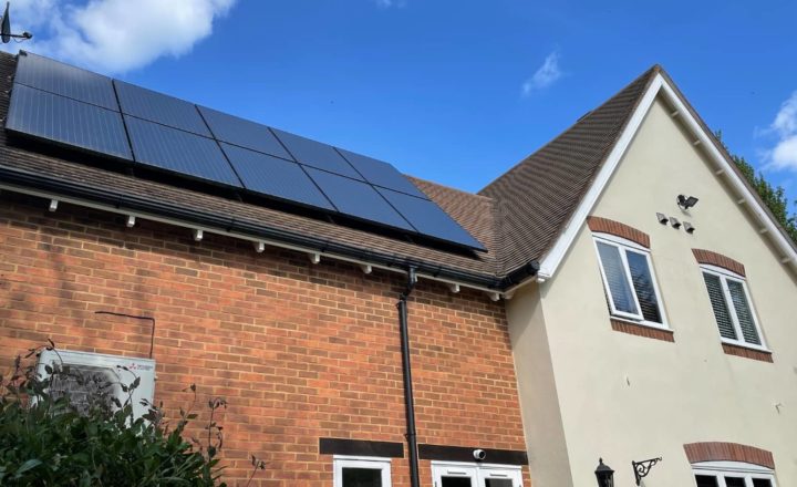 Residential house with brick and cream exterior featuring solar panels installed on the roof under a clear blue sky