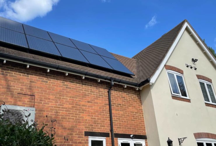 Residential house with brick and cream exterior featuring solar panels installed on the roof under a clear blue sky