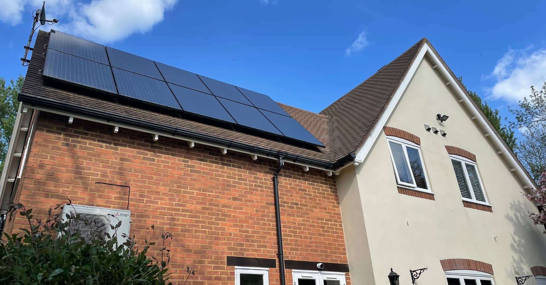 Residential house with brick and cream exterior featuring solar panels installed on the roof under a clear blue sky