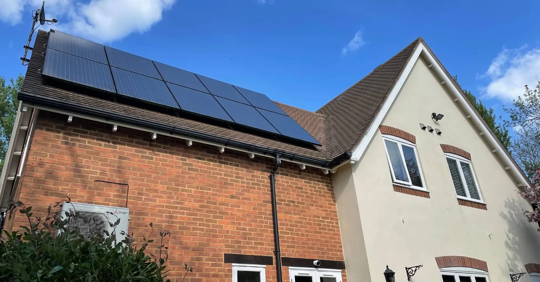 Residential house with brick and cream exterior featuring solar panels installed on the roof under a clear blue sky