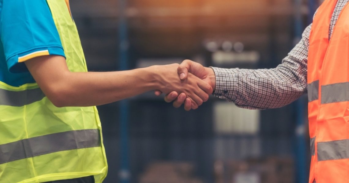 Two construction workers in hi vis jackets shake hands
