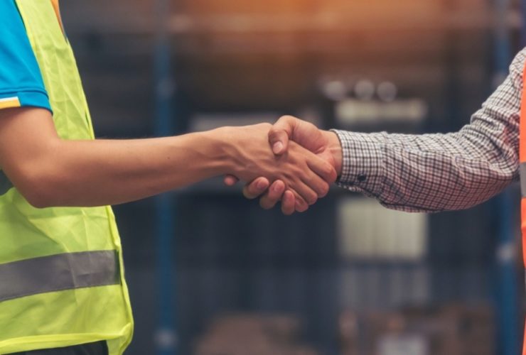 Two construction workers in hi vis jackets shake hands